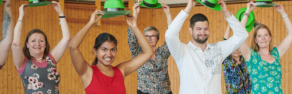 Mehrere Menschen in Tanzpose,  mit grünen Hüten